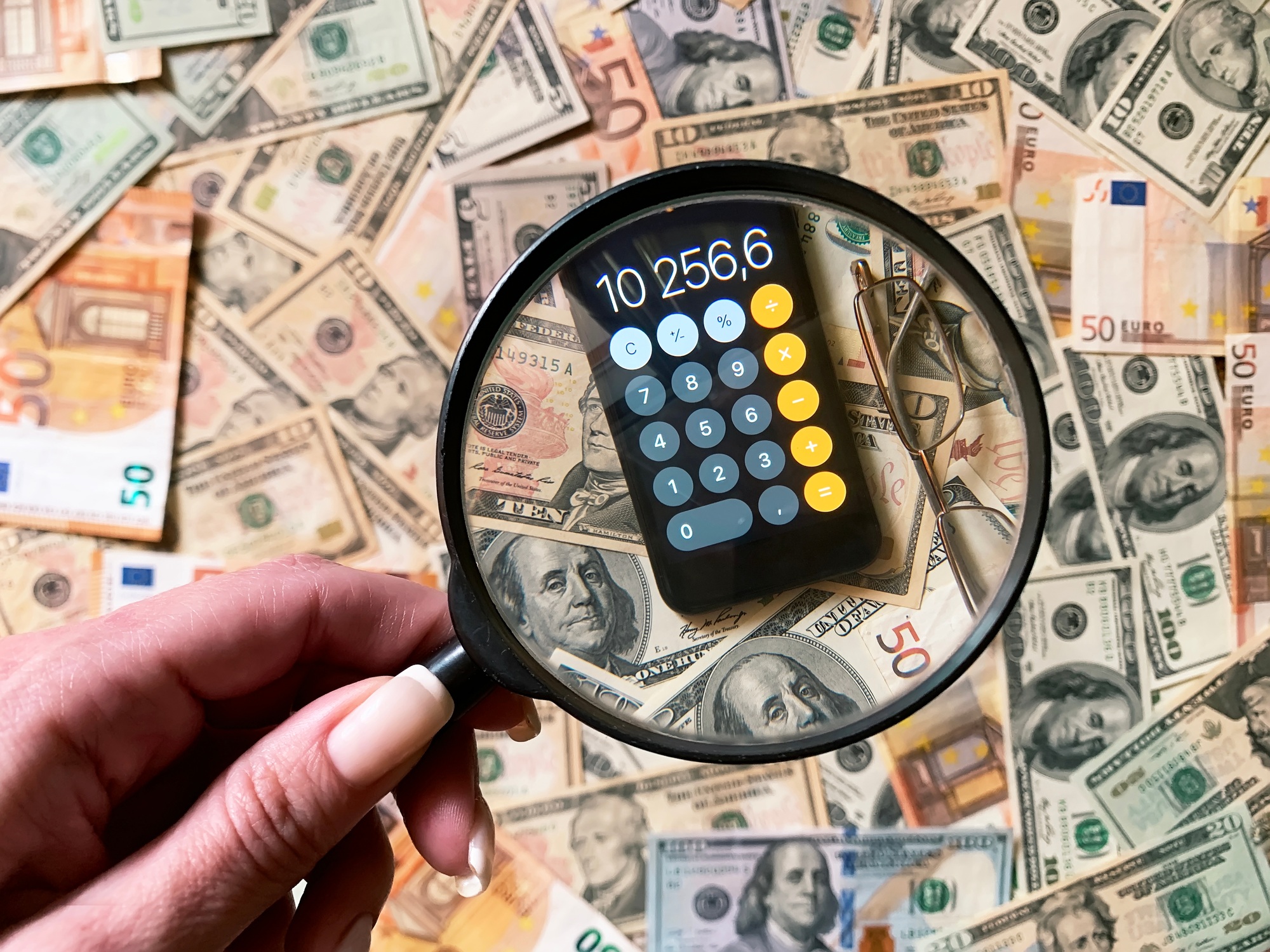 Female hand holding a magnifying glass over the mobile calculator on cash money