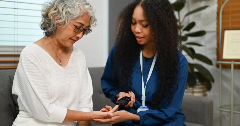 Female nurse checking blood sugar level with glucose meter of senior woman. Diabetes, health and age lifestyle concept.